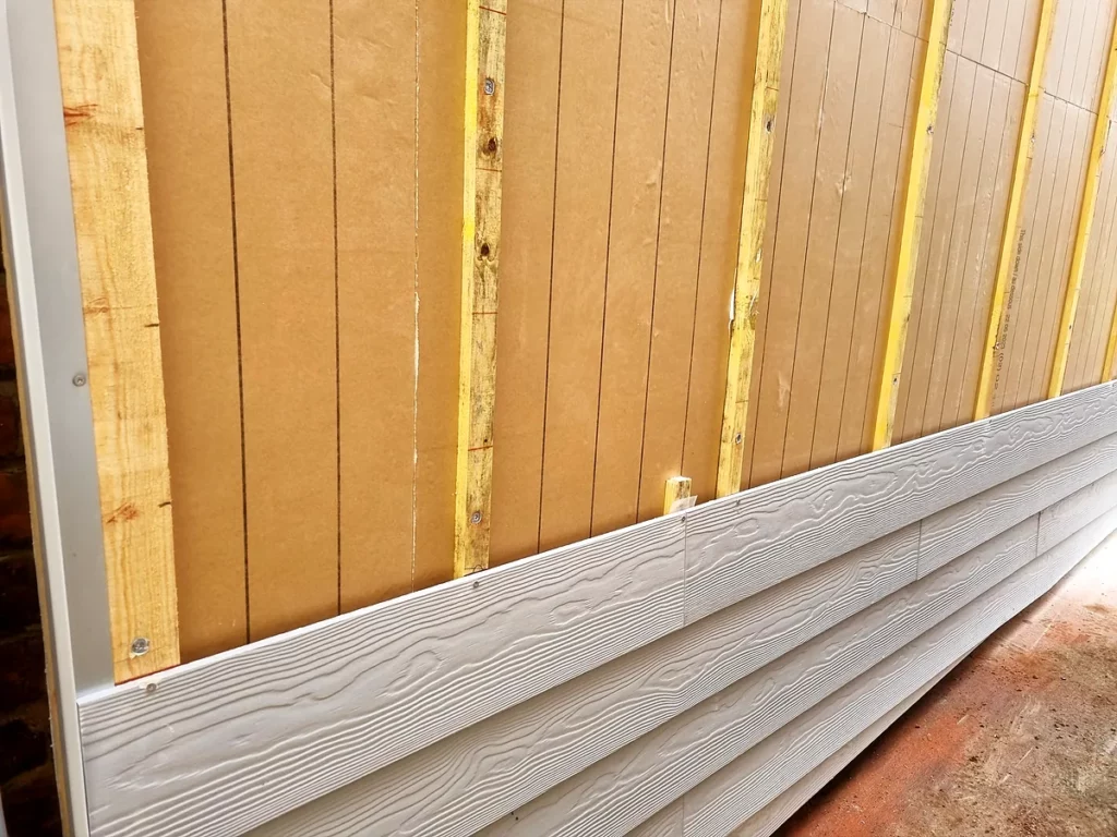 Détail de pose : lames de bardage aspect bois fixées sur tasseaux et panneau pare-pluie en fibre de bois.