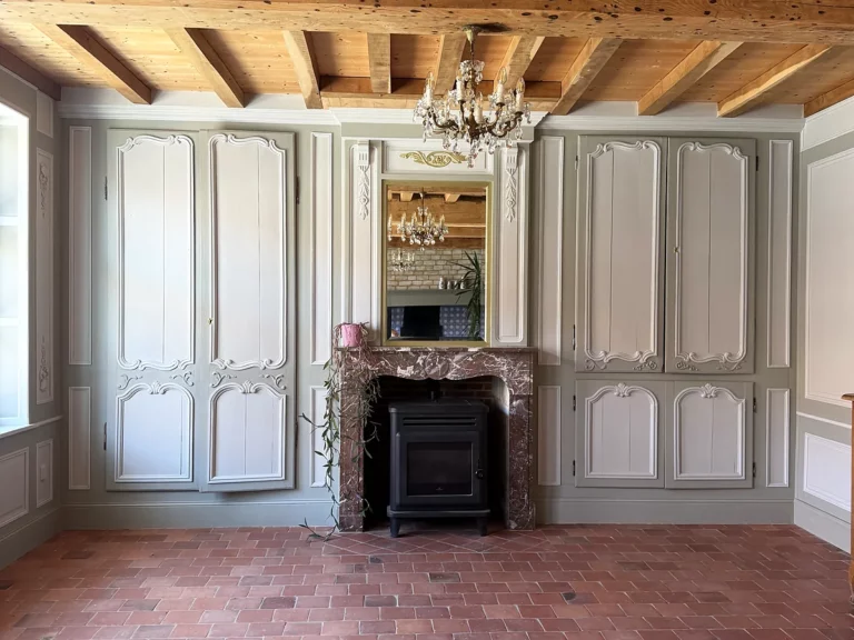 Boiseries et placards peints en gris clair à moulures sculptées encadrant une cheminée en marbre surmontée d'un miroir.