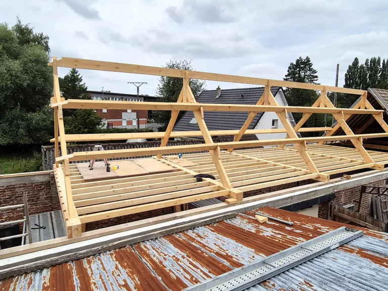 Vue d'ensemble d'une charpente neuve posée sur le mur de brique d'une maison en rénovation.