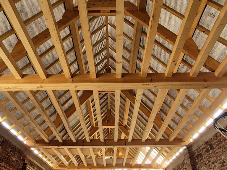 Charpente neuve à croupe d'une grange en brique, pannes et chevrons vus depuis le sol.