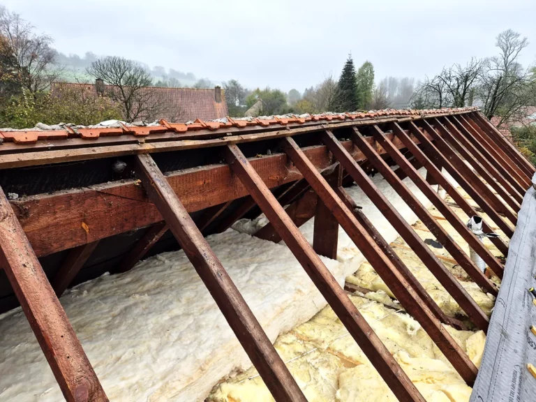 Charpente mise à nu pendant une réfection de couverture, avec la laine minérale déroulée sur le plancher du comble.