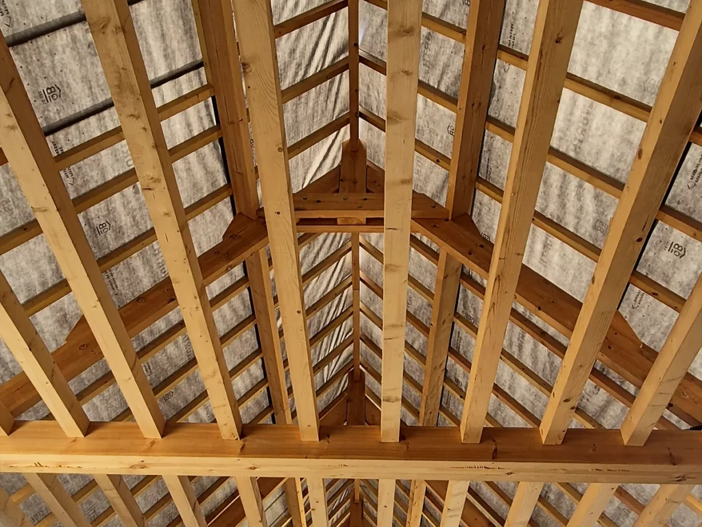 Charpente neuve d'une grange en brique : fermes, pannes et chevrons vus en contre-plongée.