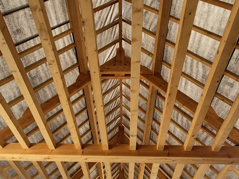 Charpente neuve d'une grange en brique : fermes, pannes et chevrons vus en contre-plongée.