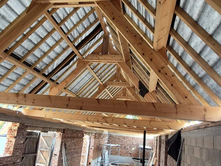 Intérieur d'une grange en rénovation avec sa charpente neuve en bois et ses murs en brique.