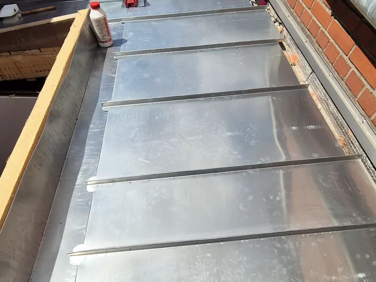 Chéneau encaissé en zinc en cours de pose entre un mur en brique et le versant de la toiture.