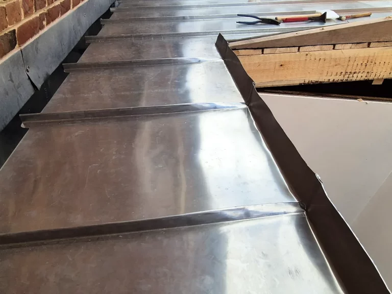 Chéneau en zinc soudé longeant un mur en brique, avec ses soudures transversales régulières.