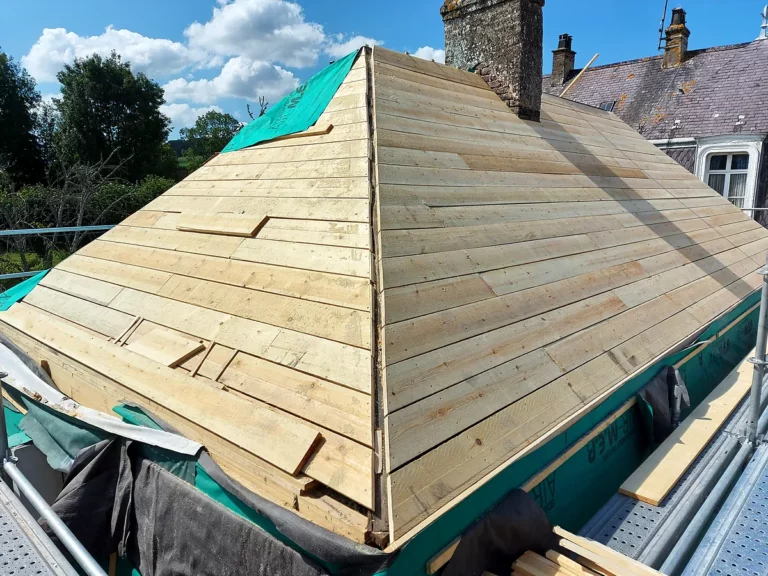 Croupe de toiture entièrement voligée en planches neuves sous un ciel bleu, prête à recevoir la couverture en ardoise.