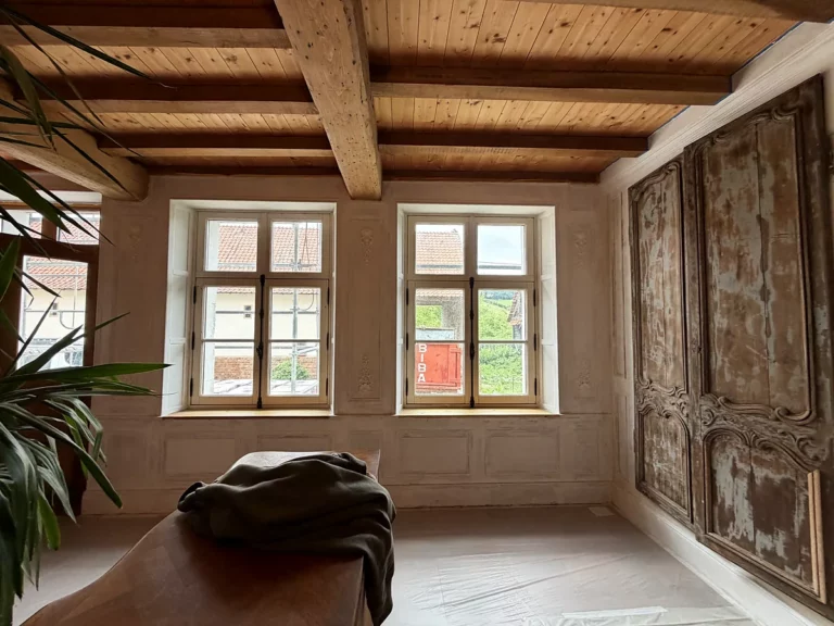 Pièce ancienne aux murs en enduit patiné et encadrements peints en trompe-l'œil, sous un plafond à la française.