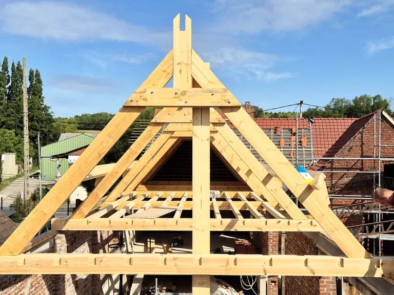 Charpentier assemblant la ferme de pignon d'une charpente neuve sur une maison en brique.