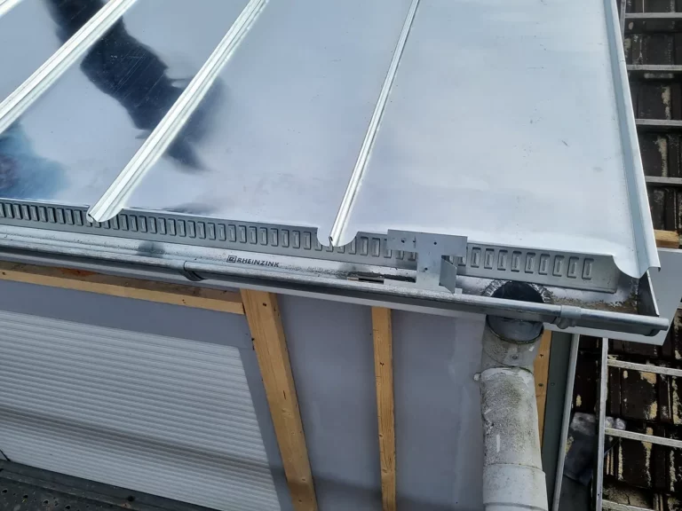 Détail du bas de pente d'une couverture en zinc à joint debout avec sa gouttière et sa descente d'eau pluviale.