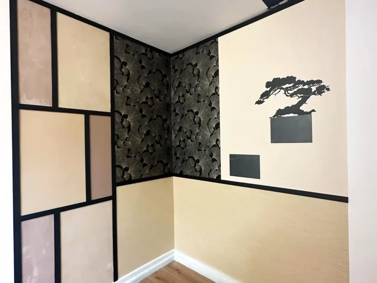 Angle de pièce habillé de panneaux d'enduit décoratif, papier peint feuillage et soubassement beige avec motif bonsaï peint.