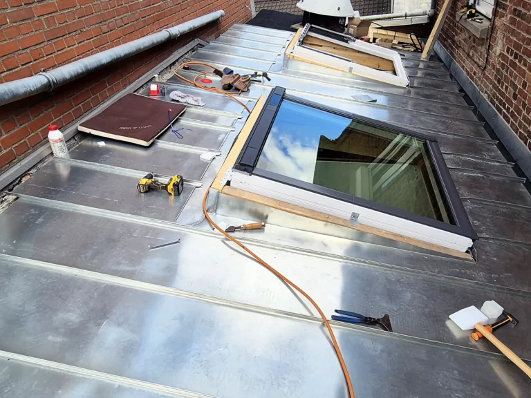 Habillage en zinc de deux fenêtres de toit sur une toiture-terrasse encadrée de murs en brique.