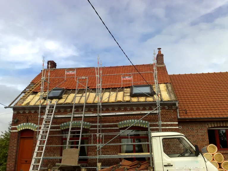 Réfection d'une couverture en tuiles avec isolant posé entre les chevrons sur une maison en brique sous échafaudage.