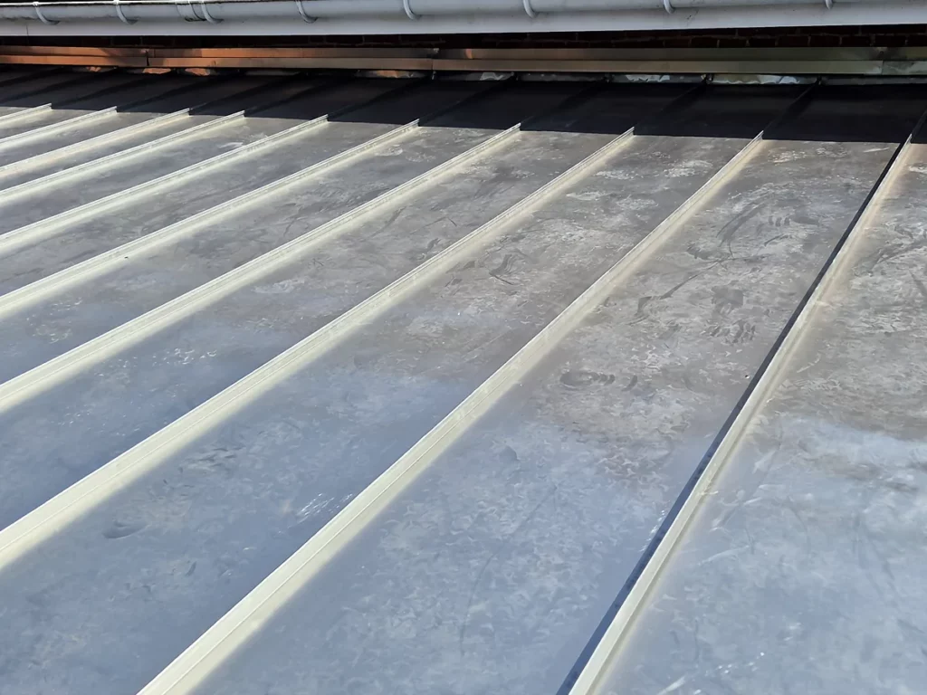 Alignement régulier des joints debout d'une couverture en zinc neuve, le long d'un mur en brique.