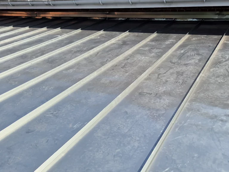 Alignement régulier des joints debout d'une couverture en zinc neuve, le long d'un mur en brique.