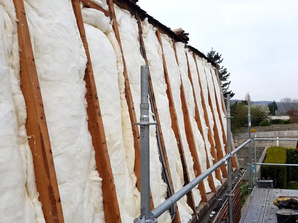 Laine de verre posée entre les chevrons d'un rampant de toiture, vue en enfilade depuis l'échafaudage du chantier.