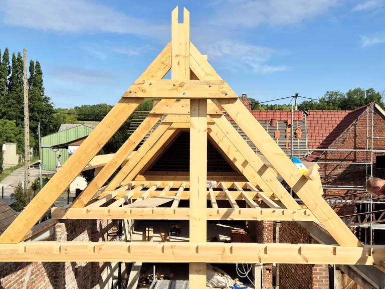Montage de la ferme de pignon d'une charpente bois neuve au-dessus d'un mur en brique.