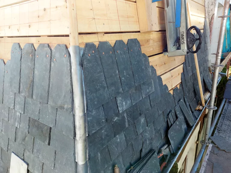 Pose des ardoises en cours de part et d'autre d'une noue en zinc façonnée, sur un voligeage neuf en planches.