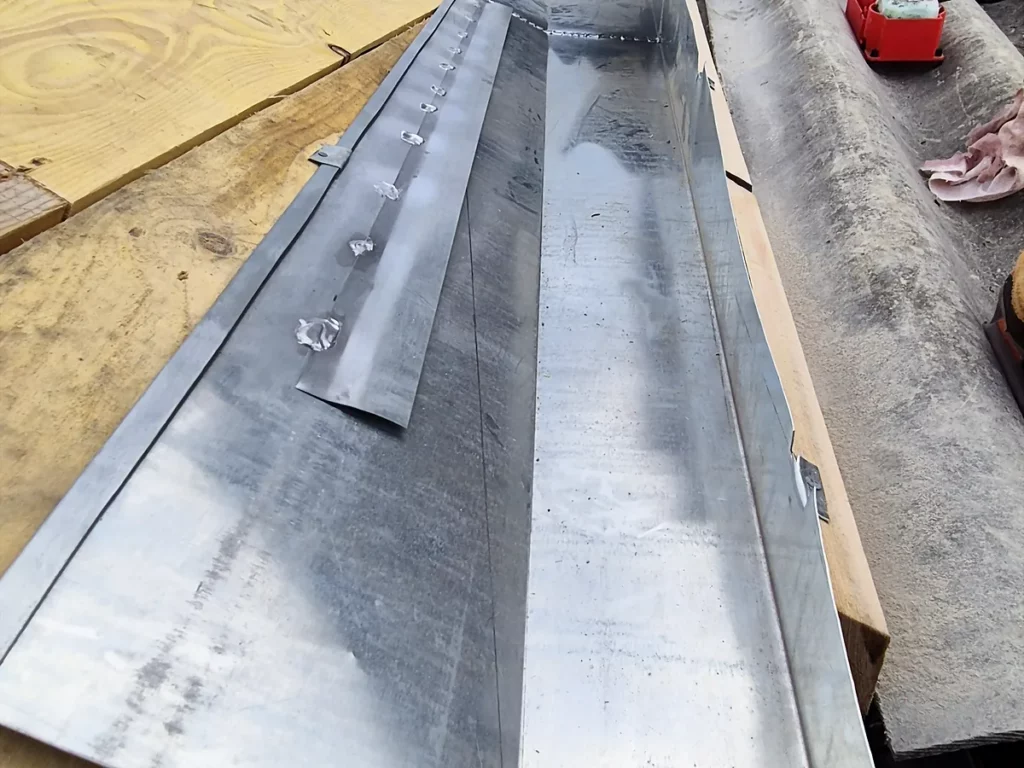 Noue en zinc façonnée posée sur voligeage, en raccord avec une couverture en plaques ondulées.