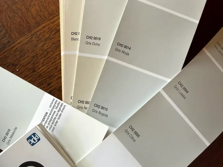Nuancier de peinture déployé en éventail sur une table en bois, montrant une gamme de gris et de beiges pour un chantier.