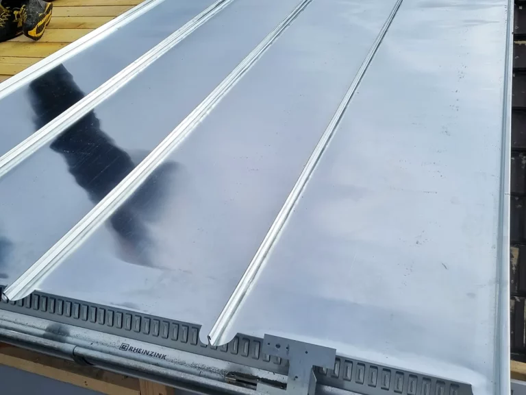 Pan de toiture en cours de couverture en zinc à joint debout, posé sur un voligeage bois neuf.
