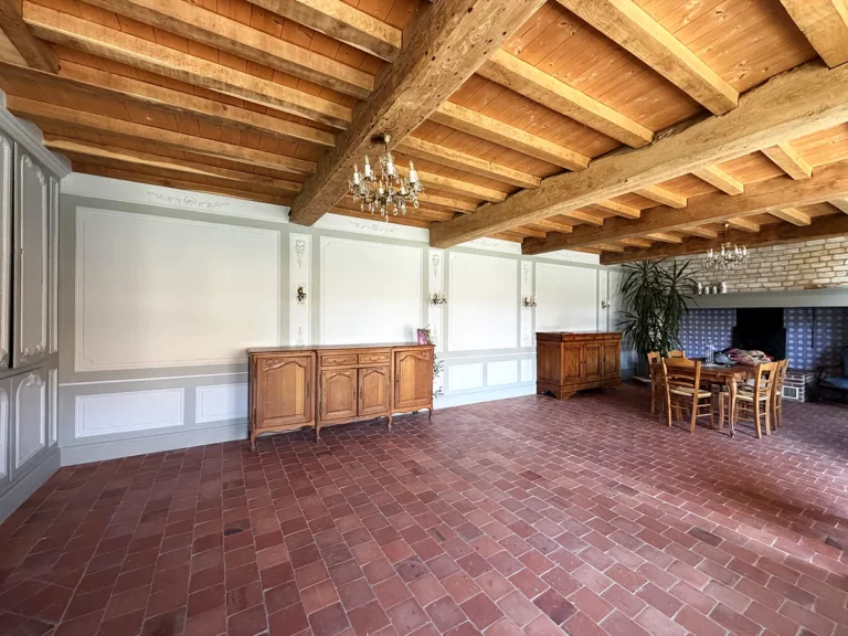 Grande salle de réception aux murs à panneaux peints gris et blanc, éclairée par deux lustres sous un plafond à poutres.