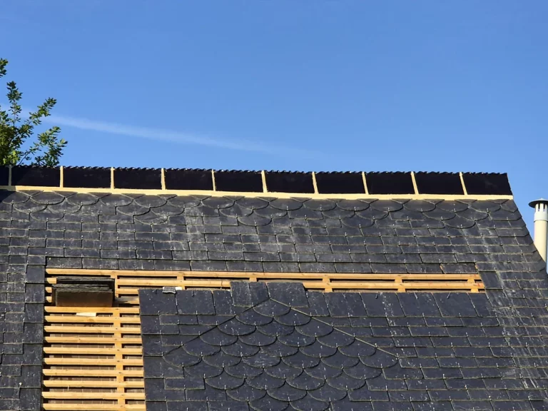 Pignon et versant en ardoise avec bande décorative à écaille, faîtage en cours de fermeture et liteaunage encore visible.