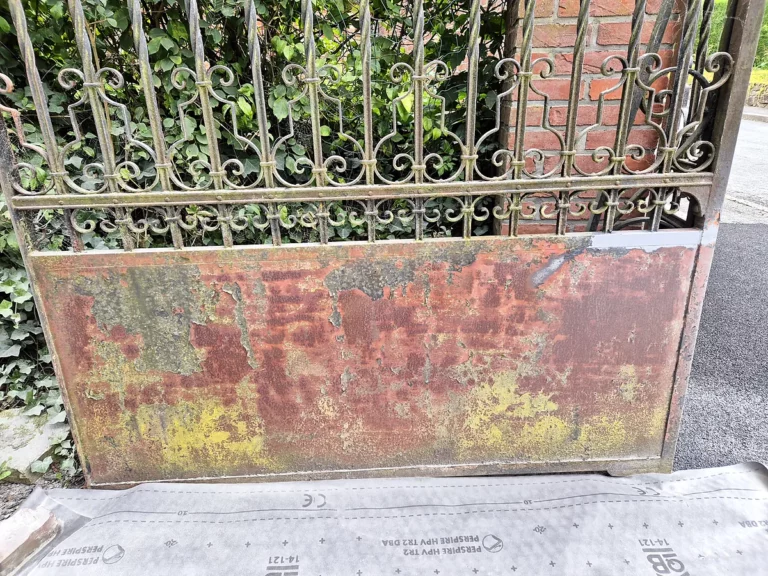 Panneau de tôle d'un portail en fer forgé rongé par la rouille et la peinture écaillée avant décapage.