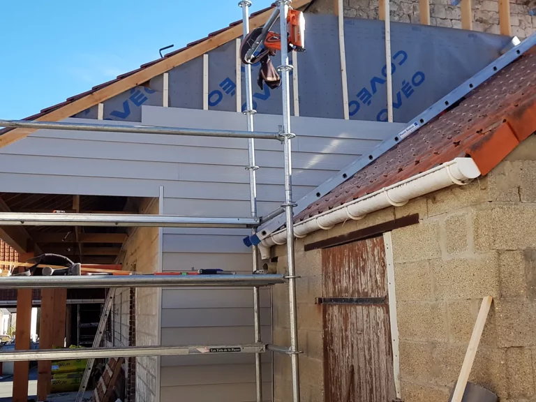 Chantier de bardage en cours sur un corps de ferme : écran pare-pluie, clins posés et gouttière zinc neuve.