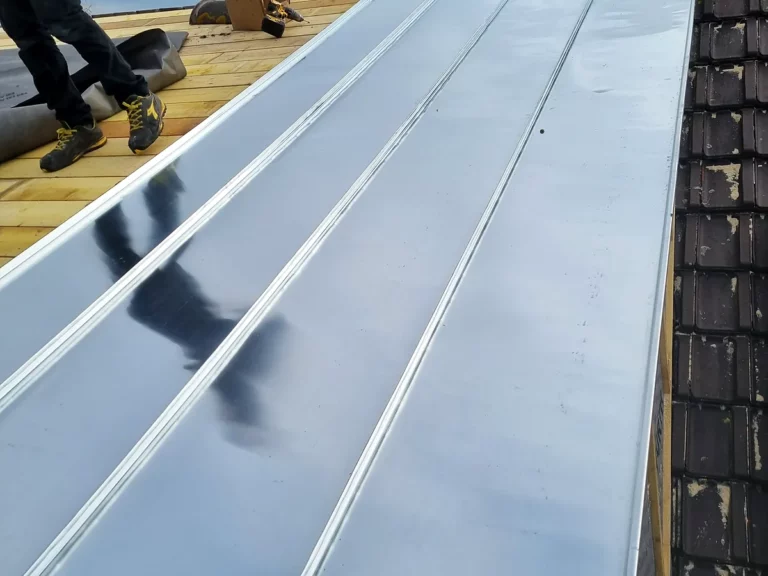 Couvreur posant des panneaux de zinc à joint debout sur un voligeage neuf lors d'une rénovation de toiture.