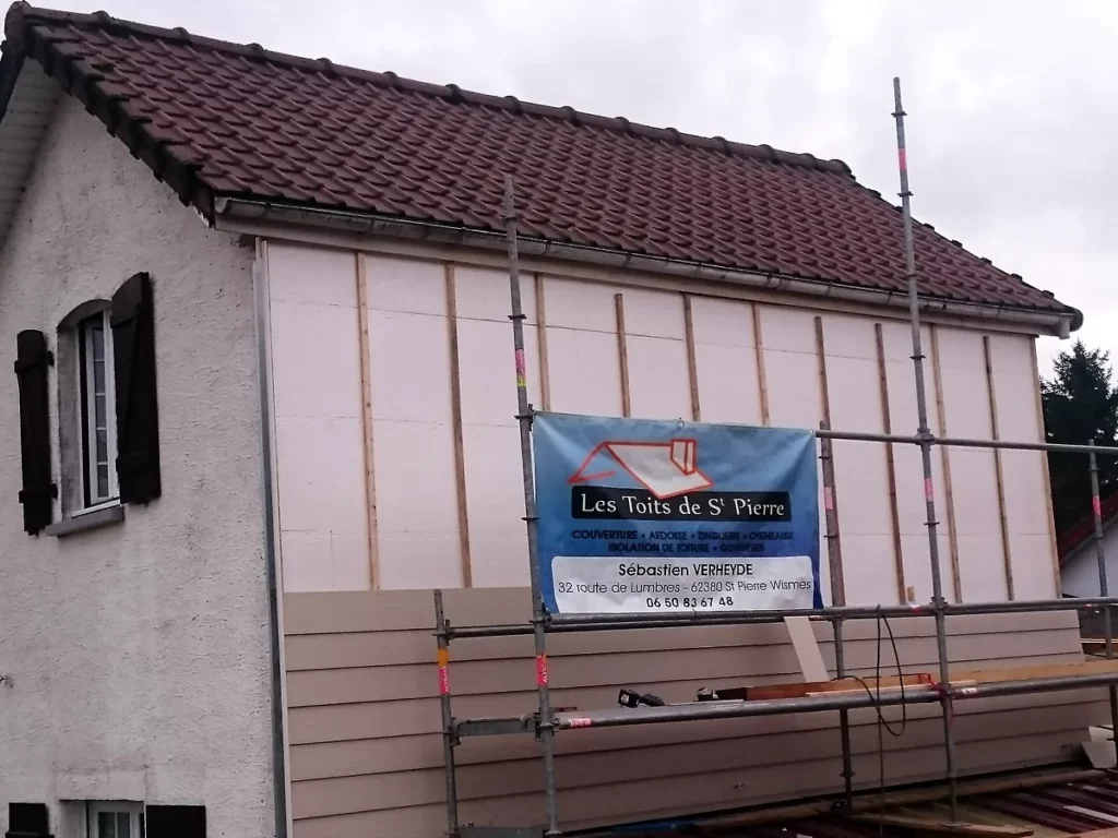 Pignon de maison en cours d'habillage : pare-pluie et tasseaux posés, premières lames de bardage en partie basse.