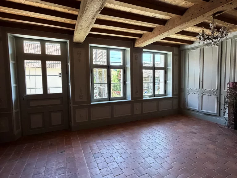 Pièce rénovée avec soubassement à panneaux peints, porte d'entrée et encadrements de fenêtres en boiserie repeinte.