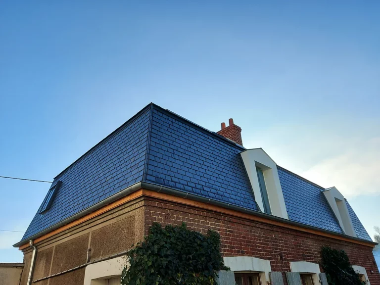 Maison en brique dont la toiture a été entièrement refaite en ardoise naturelle, avec croupe, lucarnes et souche de cheminée.
