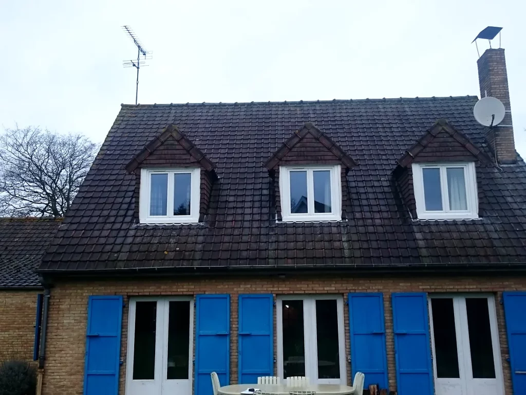 Toiture en tuiles couverte de mousse avant sa réfection complète sur une maison en briques.