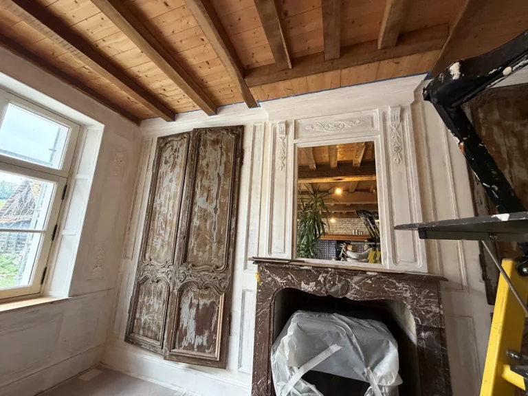 Cheminee en marbre surmontee d'un trumeau mouluré et boiseries peintes patinees, dans une piece en cours de renovation.