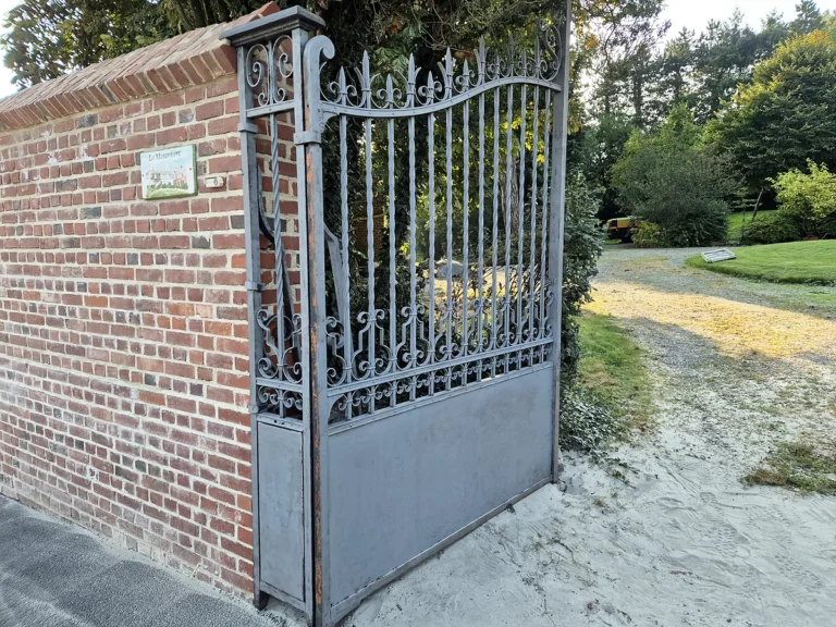 Vantail de portail en fer forgé aérogommé, acier nu prêt à être peint, le long d'un mur en briques.
