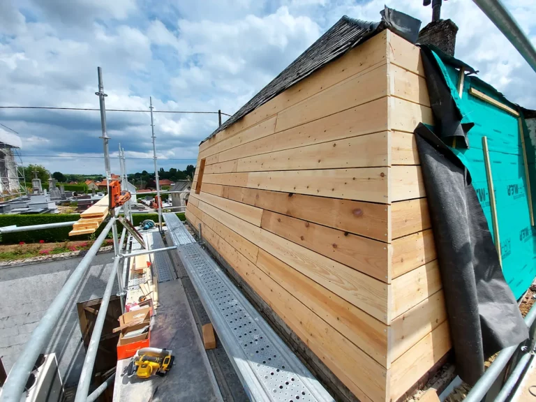Long pan de toiture et croupe entièrement voligés de planches neuves, vus depuis l'échafaudage d'un chantier de rénovation.